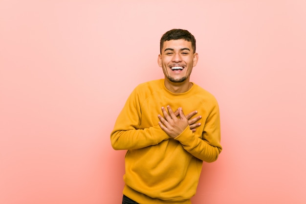 Young hispanic man laughing keeping hands on heart,  of happiness.