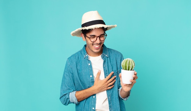 Foto giovane ispanico che ride ad alta voce per uno scherzo esilarante e tiene in mano un cactus