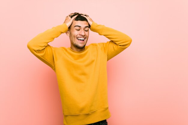 Young hispanic man laughs joyfully keeping hands on head. Happiness concept.