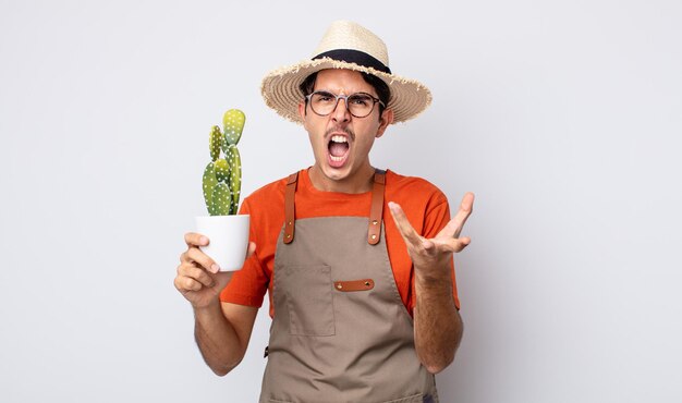 Young hispanic man looking angry, annoyed and frustrated. gardener with cactus concept