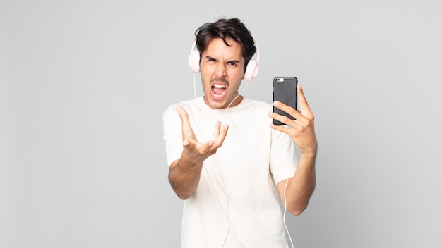 Young hispanic man looking angry, annoyed and frustrated with headphones and smartphone