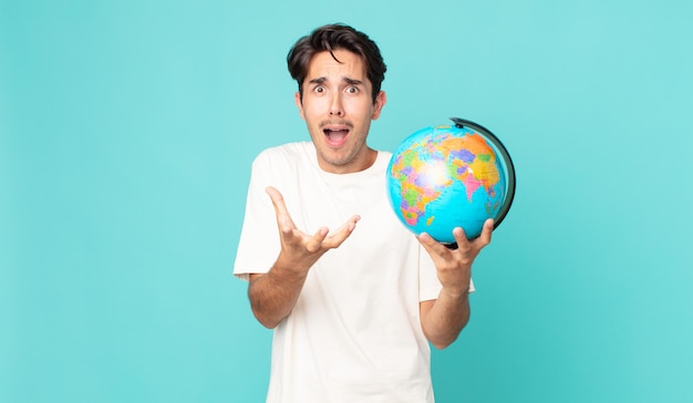 Young hispanic man looking desperate frustrated and stressed and holding a world globe map