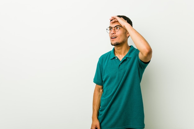 Young hispanic man looking far away keeping hand on forehead.