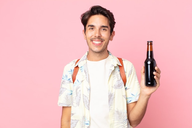 Young hispanic man looking happy and pleasantly surprised and holding a bottle of beer