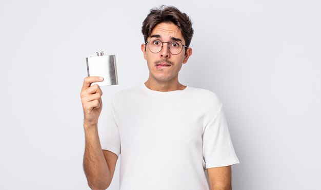 Young hispanic man looking puzzled and confused. alcohol flask concept