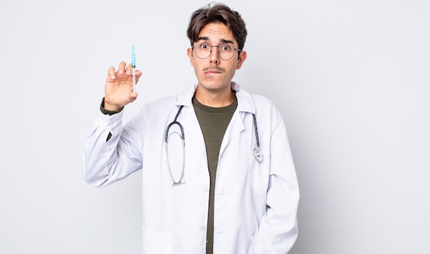 Young hispanic man looking puzzled and confused. doctor syringe concept