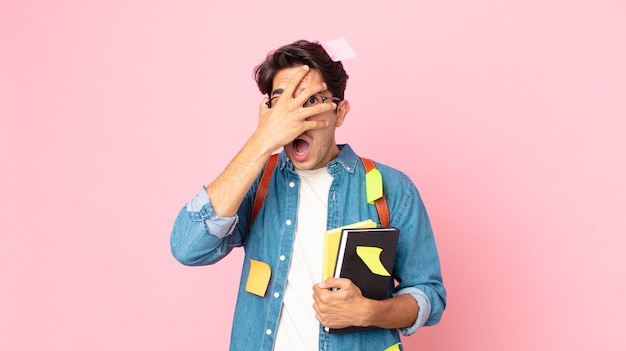 Young hispanic man looking shocked, scared or terrified, covering face with hand. student concept