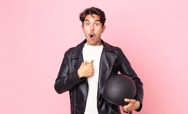 Young hispanic man looking shocked and surprised with mouth wide open, pointing to self. motorbike rider concept