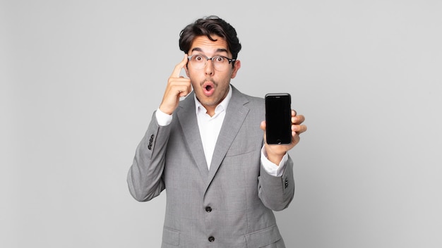 Young hispanic man looking surprised realizing a new thought idea or concept and holding a smartphone