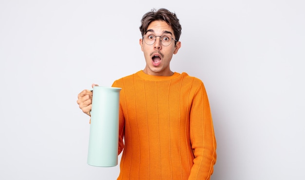 Young hispanic man looking very shocked or surprised. thermos concept