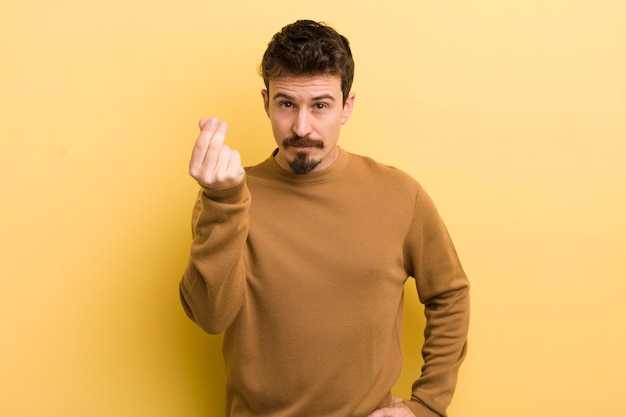 Young hispanic man making capice or money gesture telling you to pay your debts