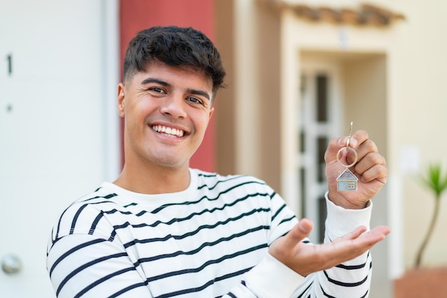 Photo young hispanic man at outdoors holding home keys with happy expression