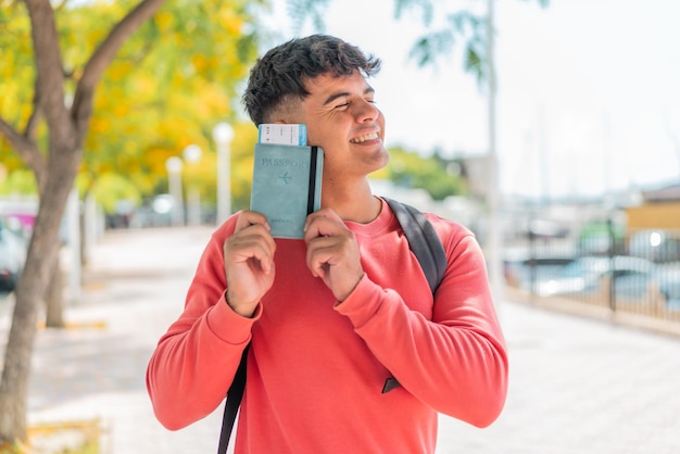 Young hispanic man at outdoors holding a passport with happy expression