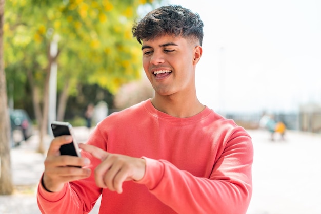 Photo young hispanic man at outdoors sending a message or email with the mobile