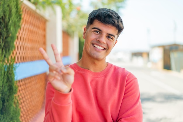 Young hispanic man at outdoors smiling and showing victory sign