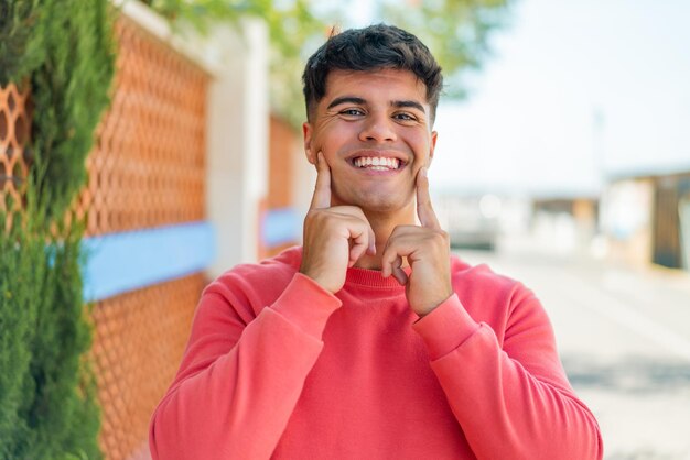 Young hispanic man at outdoors smiling with a happy and pleasant expression