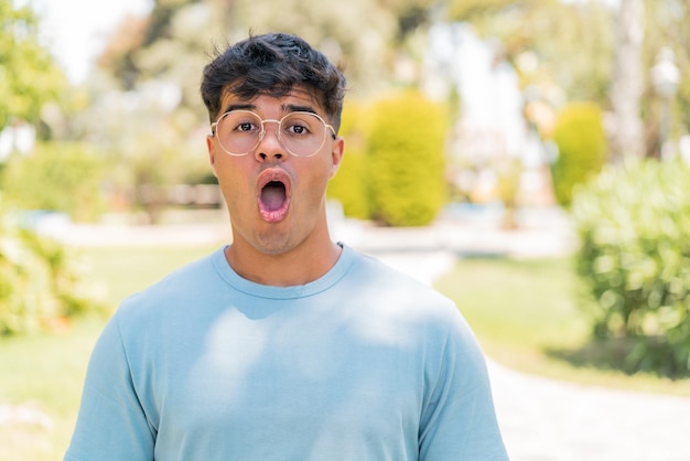 Young hispanic man at outdoors With glasses and surprised expression