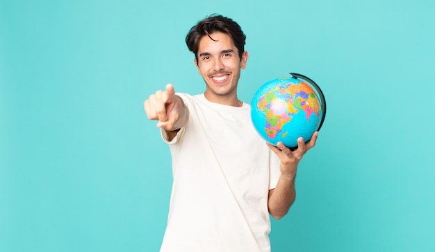 Young hispanic man pointing at camera choosing you and holding a world globe map