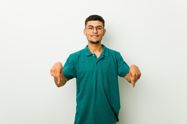 Молодой латиноамериканский мужчина указывает вниз пальцами, позитивные чувства.