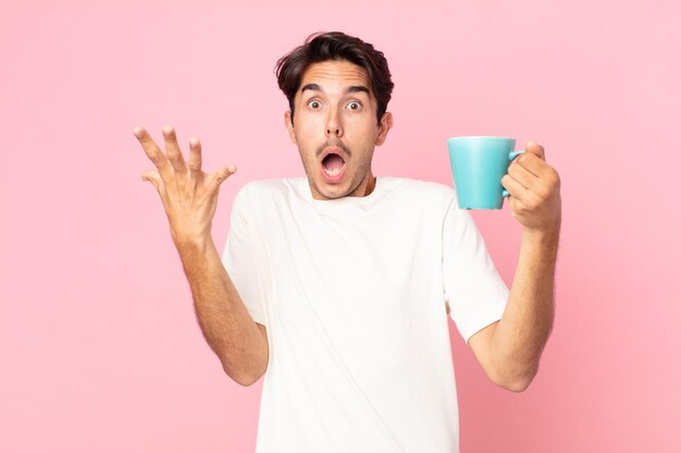 young hispanic man screaming with hands up in the air and holding a coffee mug