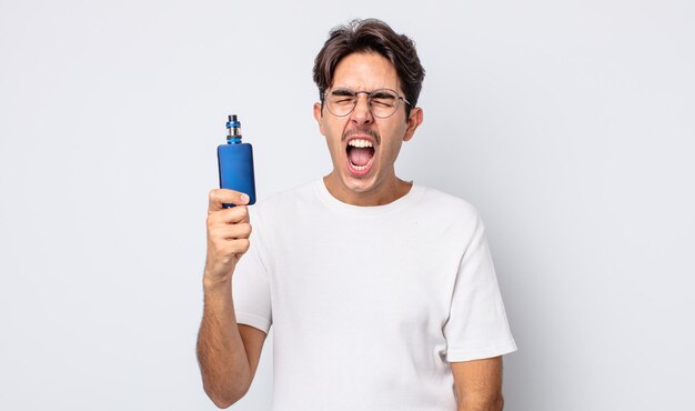 Young hispanic man shouting aggressively, looking very angry. smoke vaporizer concept