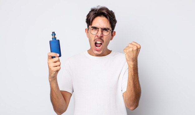 Young hispanic man shouting aggressively with an angry expression. smoke vaporizer concept