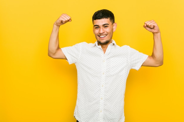 Young hispanic man showing strength gesture with arms, symbol of feminine power