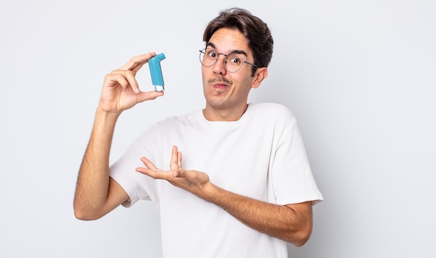 Young hispanic man shrugging, feeling confused and uncertain. asthma concept