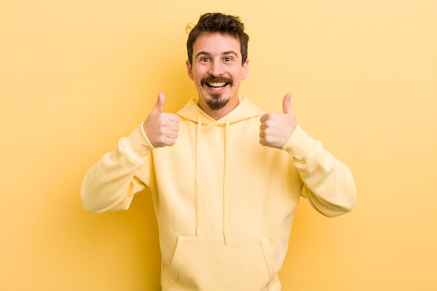 Young hispanic man smiling broadly looking happy positive confident and successful with both thumbs up