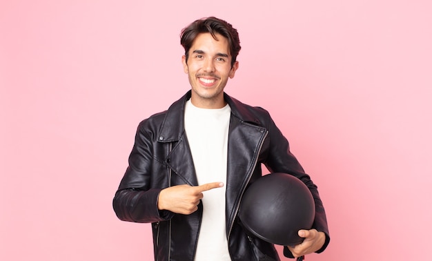 Young hispanic man smiling cheerfully, feeling happy and pointing to the side. motorbike rider concept