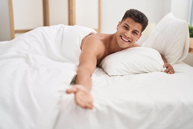 寝室のベッドに横たわって自信を持って微笑む若いヒスパニック系男性