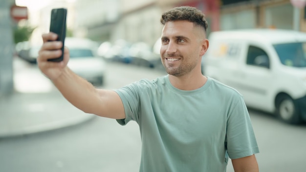 Young hispanic man smiling confident making selfie by the smartphone at street