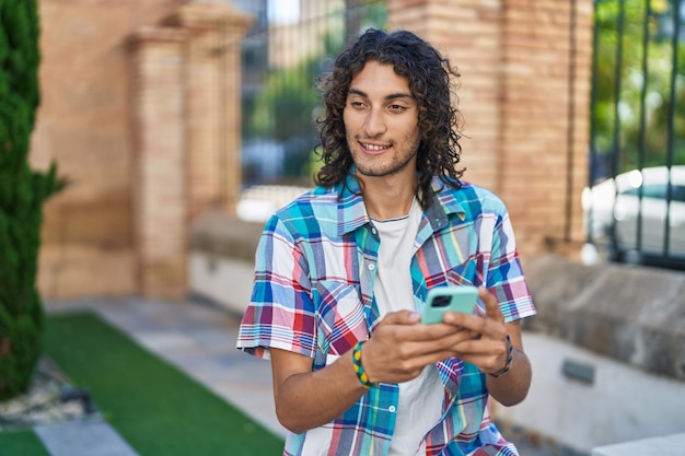 通りでスマートフォンを使って自信を持って微笑む若いヒスパニック系男性