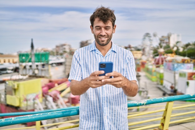 Young hispanic man smiling happy using smartphone at the attraction park