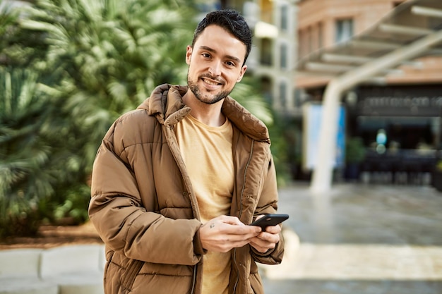 街でスマートフォンを使って幸せな笑みを浮かべている若いヒスパニック系男性