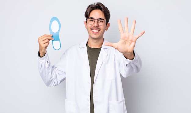young hispanic man smiling and looking friendly, showing number five. chiropodist concept