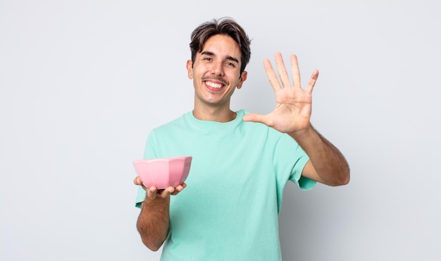 Young hispanic man smiling and looking friendly, showing number five. empty bowl concept