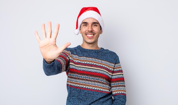 젊은 히스패닉 남자가 웃고 친절해 보이며 5번을 보여줍니다. 새해와 크리스마스 컨셉