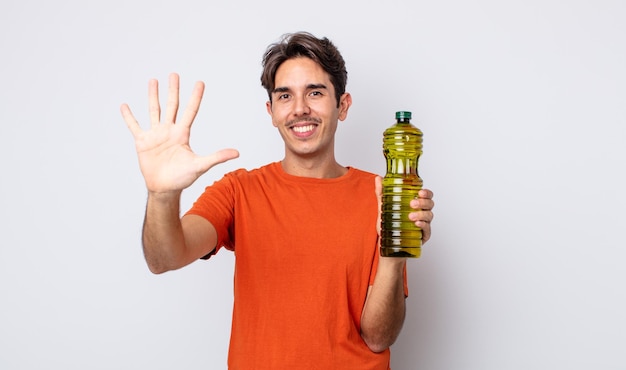 Young hispanic man smiling and looking friendly, showing number five. olive oil concept