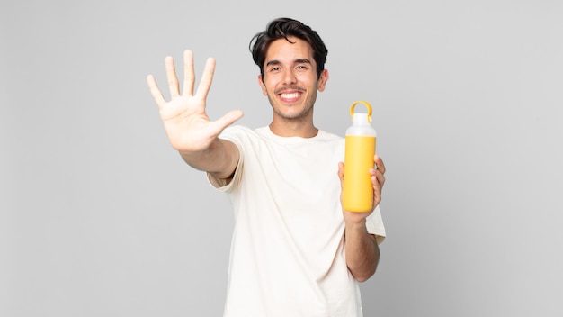 Young hispanic man smiling and looking friendly, showing number five with a coffee thermos