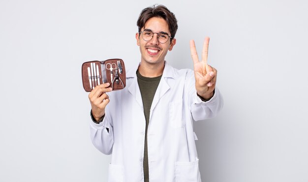 Giovane uomo ispanico che sorride e che sembra amichevole, mostrando il numero due. strumenti per unghie podologo