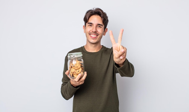 Young hispanic man smiling and looking friendly, showing number two. cookies concept