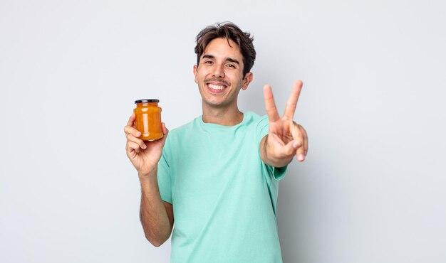 Young hispanic man smiling and looking happy, gesturing victory or peace. peach jelly concept