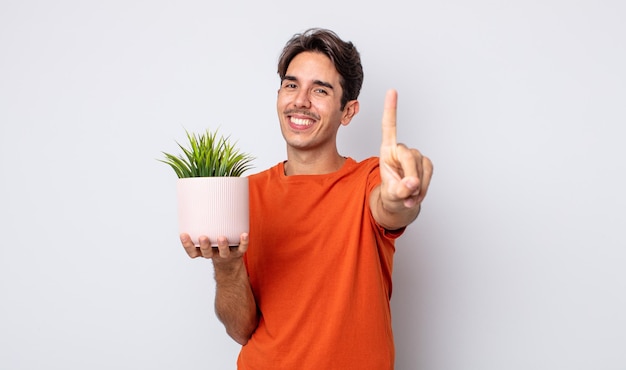 Young hispanic man smiling proudly and confidently making number one. decorative plant concept