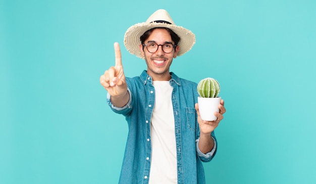 young hispanic man smiling proudly and confidently making number one and holding a cactus