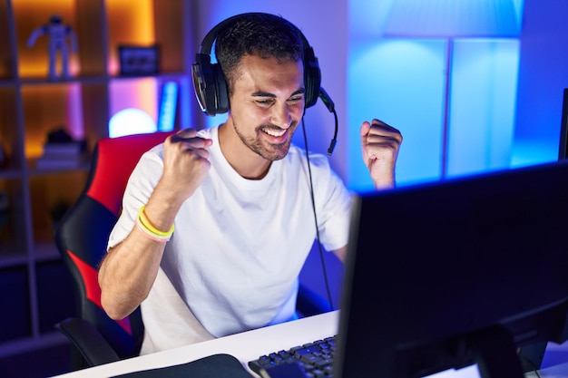 Young hispanic man streamer playing video game with winner expression at gaming room