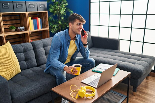 Young hispanic man student talking on smartphone drinking coffee at home