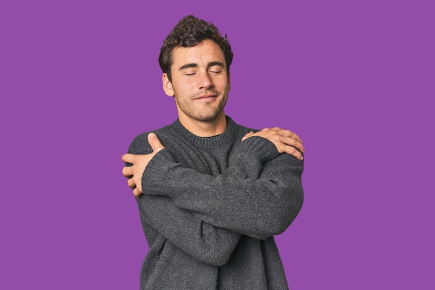 Young Hispanic man in studio hugs smiling carefree and happy