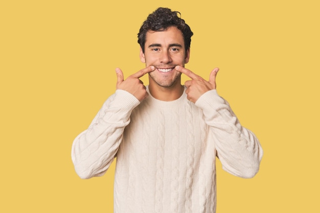 Photo young hispanic man in studio smiles pointing fingers at mouth