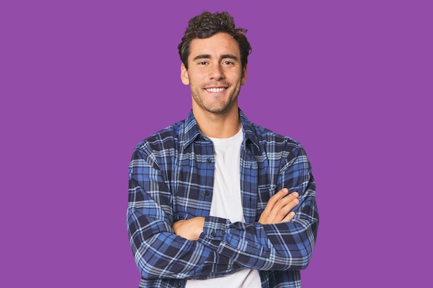 young hispanic man in studio who feels confident crossing arms with determination